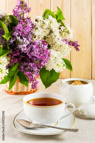 Cup of tea and branch of lilac flower on linen tablecloth