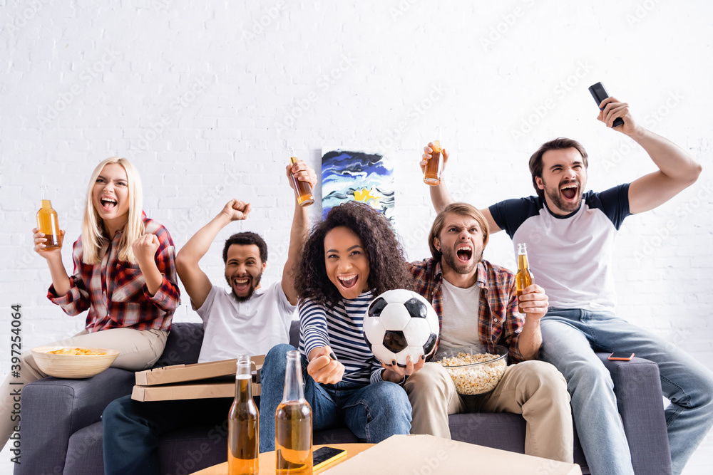 excited multiethnic friends showing win gesture while watching football championship at home