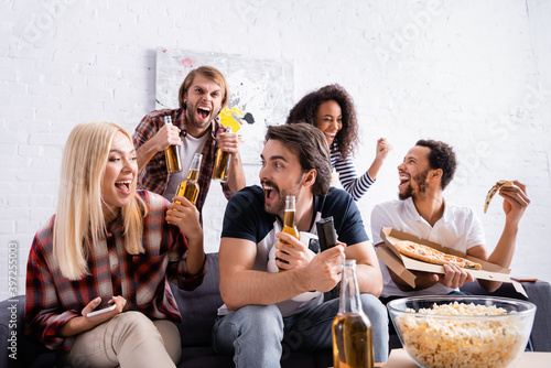 excited sports fans holding bottles of beer while watching competition at home