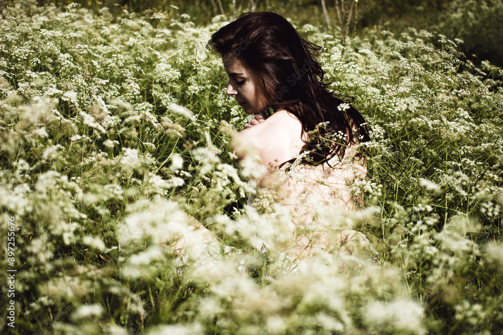 Naklejka premium Young woman with black hair and naked back among wildflowers 