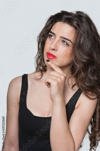 Thoughtful young woman looking away with hand on chin over gray background