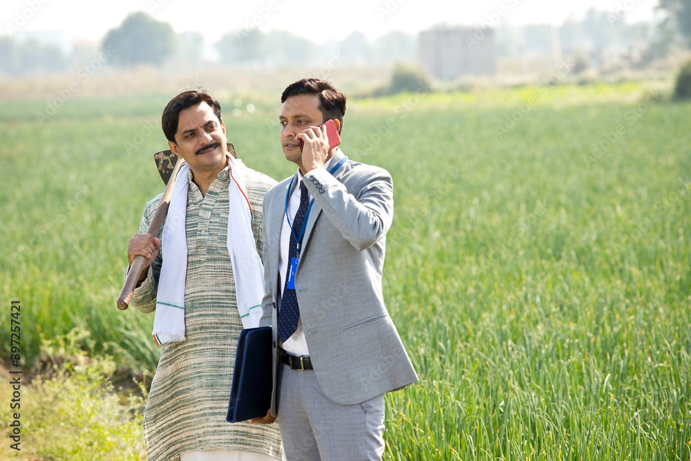 Businessman using phone while discussing with farmer on agriculture field Businessman using phone while discussing with farmer on agriculture field