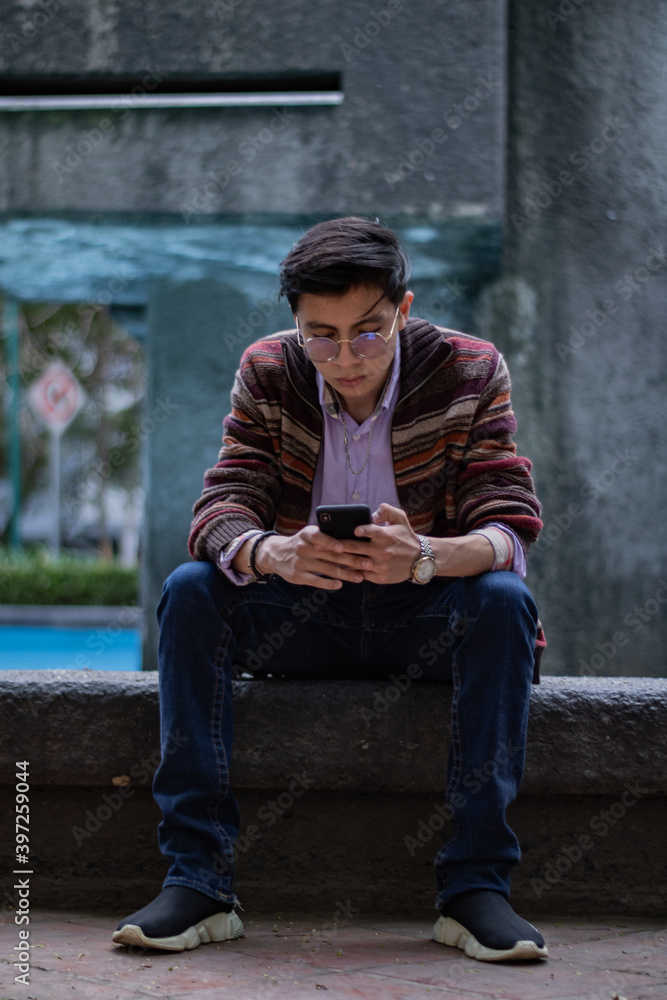 young man using cell phone sitting in front of a fountain young man using cell phone sitting in front of a fountain