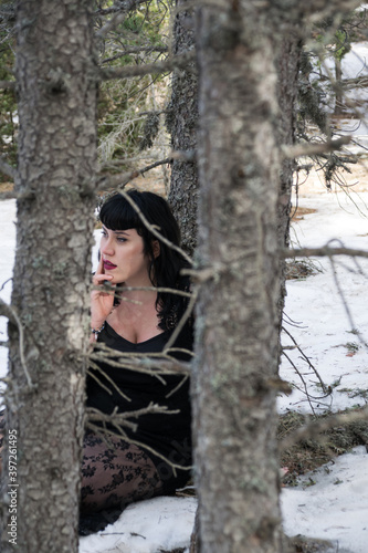View of a woman through the trees sitting in the snow in a black dress