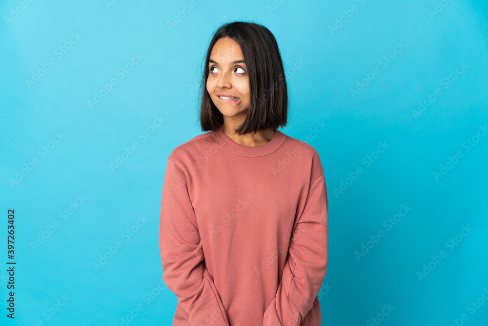 Fototapeta premium Young latin woman isolated on blue background having doubts while looking up