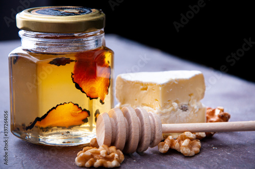 Jar of raw honey infused with truffle. A delicious accompaniment to breakfast or snack served with brie cheese and garnished with walnuts.
