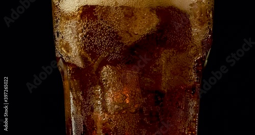 Truck shot of pouring carbonated drinks bubbles with ice cubes. Pouring soft drinks with ice and bubbles in glass on black background.