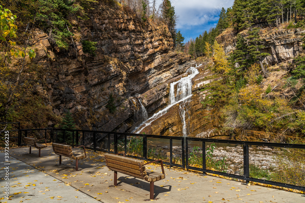 Obraz premium Cameron falls in autumn sunny day morning. Blue sky, white clouds over mountains in the background. Waterton Lakes National Park, Alberta, Canada.