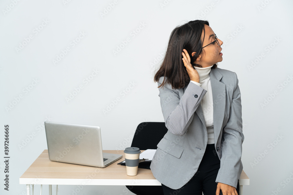 Young latin business woman working in a office isolated on white background listening to something by putting hand on the ear Young latin business woman working in a office isolated on white background listening to something by putting hand on the ear