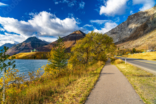 Middle Waterton Lake lakeshore in autumn foliage season sunny day morning. Blue sky, white clouds over mountains in the background. Landmarks in Waterton Lakes National Park, Alberta, Canada.