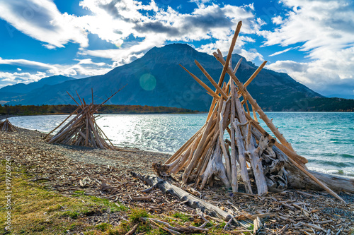 Driftwood Beach, Middle Waterton Lake lakeshore in autumn foliage season morning. Blue sky, white clouds over mountains in the background. Landmarks in Waterton Lakes National Park, Alberta, Canada. © Shawn.ccf