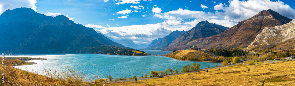 Middle Waterton Lake lakeshore in autumn foliage season sunny day morning. Blue sky, white clouds over mountains in the background. Landmarks in Waterton Lakes National Park, Alberta, Canada.