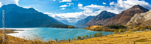 Middle Waterton Lake lakeshore in autumn foliage season sunny day morning. Blue sky, white clouds over mountains in the background. Landmarks in Waterton Lakes National Park, Alberta, Canada.