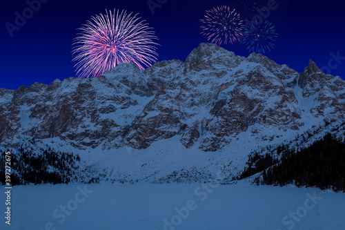 Fototapeta Naklejka Na Ścianę i Meble -  Celebratory fireworks for new year over Tatra National Park, Zakopane Poland. Famous Mountains Lake Morskie Oko Or Sea Eye during last night of year. Christmas atmosphere. Snow above it and mountain 