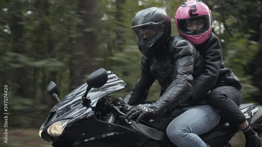 Side view of young couple of bikers wearing helmets and leather jackets riding motorcycle outdoors. Confident man and woman driving motorbike on cloudy day outdoors. Lifestyle and leisure concept. Side view of young couple of bikers wearing helmets and leather jackets riding motorcycle outdoors. Confident man and woman driving motorbike on cloudy day outdoors. Lifestyle and leisure concept.