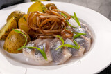 Seafood. Slices of lightly salted herring with baked potatoes and pickled onions on a white plate and dark background