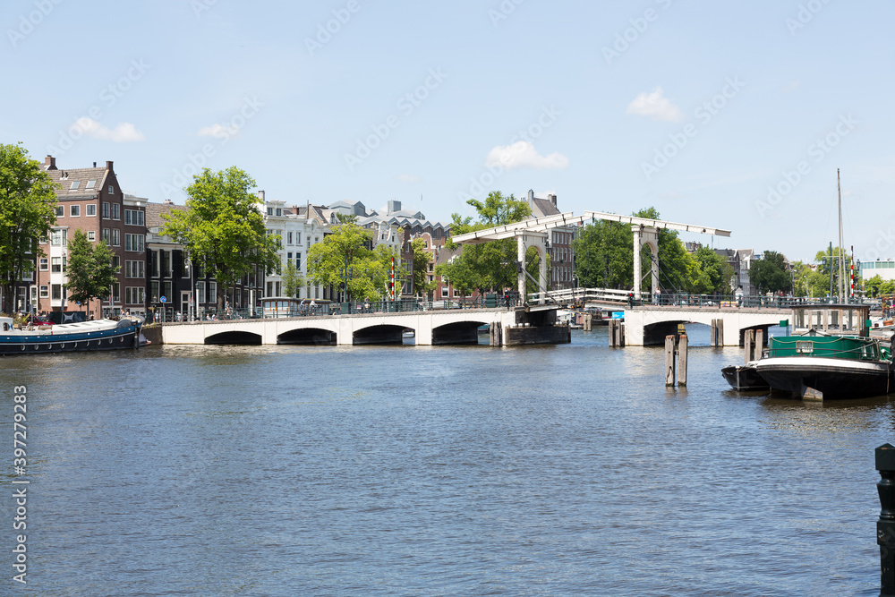 View of Amstel River in the city center of Amsterdam. Seen from Roeterseiland with canal houses, canal boats, Schutssluis.