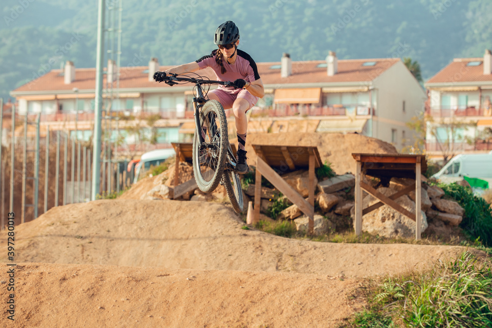 Sportswoman in black helmet and sportswear with glasses riding mountain bike jumping from a bridge in training track Sportswoman in black helmet and sportswear with glasses riding mountain bike jumping from a bridge in training track