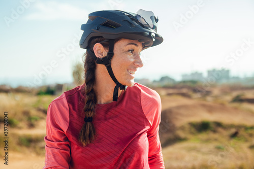 Sportswoman in black helmet and red sportswear with glasses resting near training track looking away photo