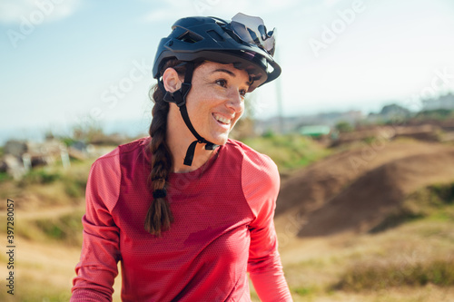 Sportswoman in black helmet and red sportswear with glasses resting near training track looking away photo