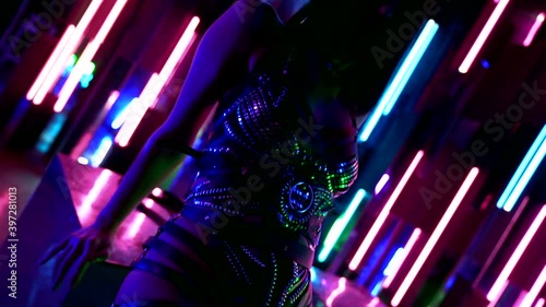 Close-up of a toned woman in heels in beautiful strappy underwear, passionately posing against walls with colorful neon lights on stage sitting on reflective cubes. photo