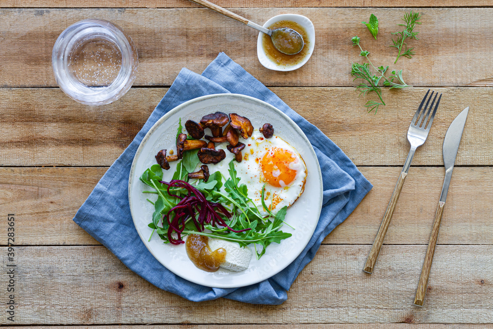 Top view of plate with palatable fried egg served with mushrooms and fresh salad on wooden table with sauce and glass of water Top view of plate with palatable fried egg served with mushrooms and fresh salad on wooden table with sauce and glass of water