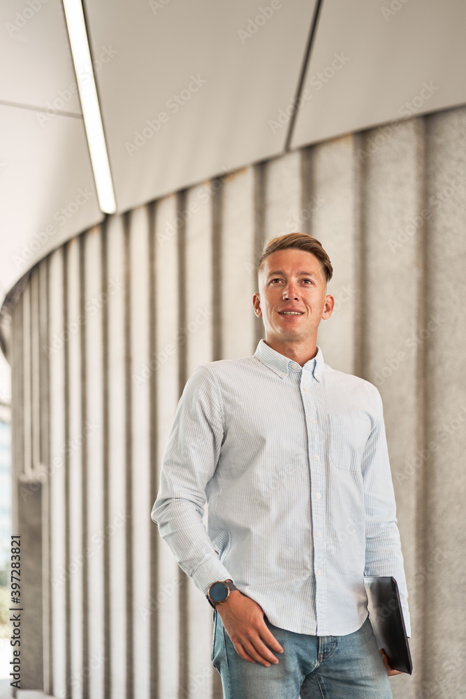 Low angle of confident male entrepreneur in smart casual outfit standing in city with netbook and looking away Low angle of confident male entrepreneur in smart casual outfit standing in city with netbook and looking away