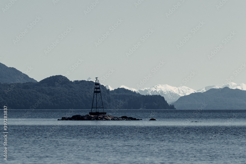 Picturesque view of metal tower on rock in sea on background of highlands covered with snow in Patagonia Picturesque view of metal tower on rock in sea on background of highlands covered with snow in Patagonia