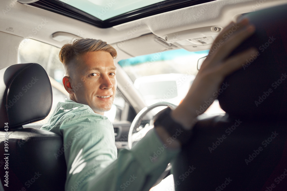 Side view of handsome smiling male driver sitting in parked luxury car and looking at camera Side view of handsome smiling male driver sitting in parked luxury car and looking at camera