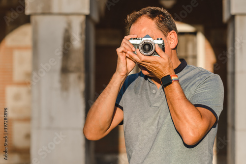 Unrecognizable male photographer covering face with retro photo camera and taking photo on sunny day on street photo