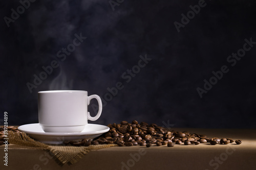 Coffee cup with saucer and scattered coffee beans on dark background. Space for text