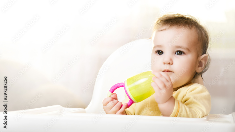 Little baby sitting in high chair and eating food indoors.. baby's first feeding. 6 month old toddler with nibbler in hand Little baby sitting in high chair and eating food indoors.. baby's first feeding. 6 month old toddler with nibbler in hand