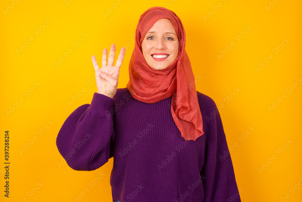 Young caucasian Muslim woman wearing hijab standing against yellow wall showing and pointing up with fingers number four while smiling confident and happy. Young caucasian Muslim woman wearing hijab standing against yellow wall showing and pointing up with fingers number four while smiling confident and happy.