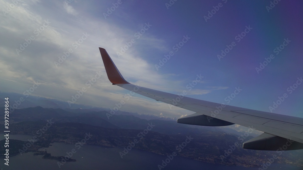 Obraz premium Wing of an airplane flying above the evening clouds and earth surface, looking out the window of a plane. Aerial view from a flying plane in the sky over
