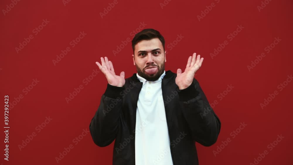 Shocked bearded man looking at camera with scared face on red wall background. Shocked bearded man looking at camera with scared face on red wall background.