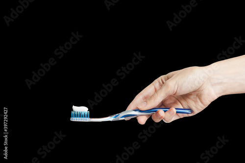 hand of a woman holding toothbrush with toothpaste isolated on black background. Female hand with blue tooth brush