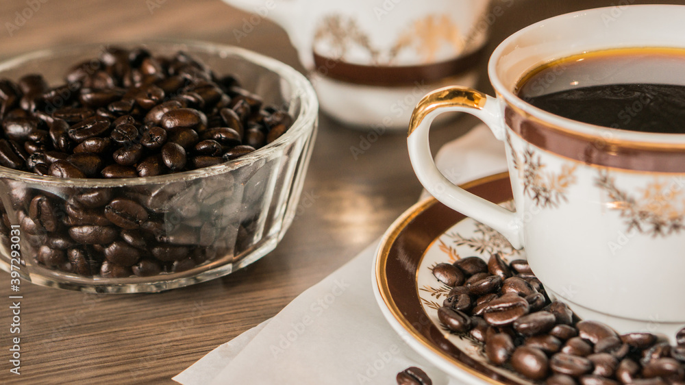 Fototapeta premium Cup of coffee and coffee beans on white paper on old wooden background