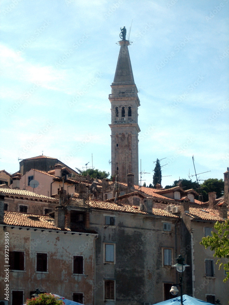 The tall tower of the city hall rises above the tiled roofs of houses in an ancient European city.