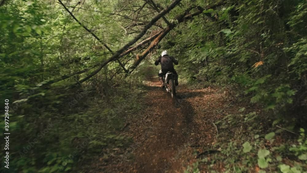Tracking slowmo of unrecognizable man in helmet riding motorcycle through forest Tracking slowmo of unrecognizable man in helmet riding motorcycle through forest