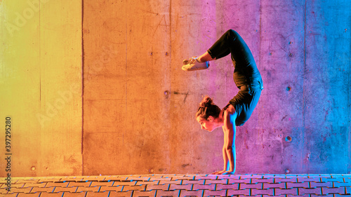 Woman practicing gymnastic in multi colored light against wall photo