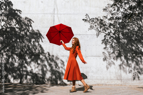 Woman in red dress holding red umbrella while standing against tree shadow wall photo