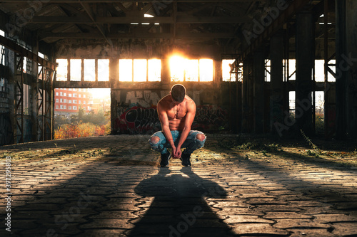 Fitness man posing in a ruined industry pavillion with the sunlight at the back. © Jorge Argazkiak