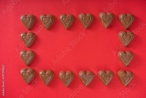 Chocolate hearts frame over red background top view copy space