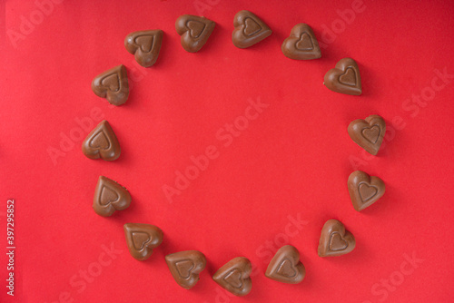 Chocolate hearts frame over red background top view copy space
