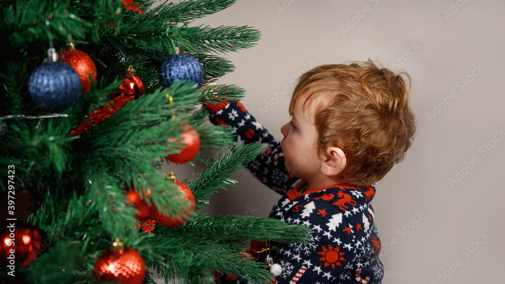 A child with a Christmas tree. A little blond boy reaches for the toy on a beautiful green Christmas tree. Christmas photo A child with a Christmas tree. A little blond boy reaches for the toy on a beautiful green Christmas tree. Christmas photo
