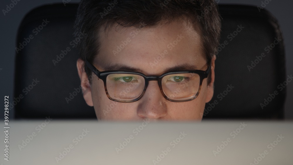 Closeup of man eyes in eyeglasses in front of the computer in home office  on background of grey wall. Young man sitting at home working alone at  night Photos | Adobe Stock