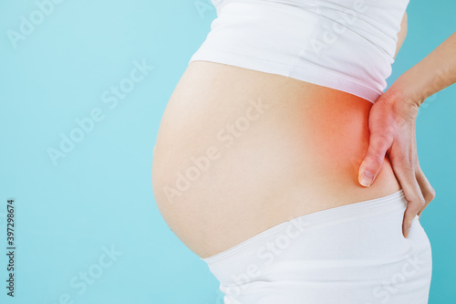 Pregnant woman with back pain isolated on blue background with copy space.