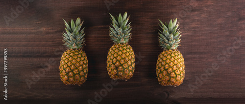 Three 3 ripe pineapples together on a wooden brown table  with a cinematic styple aspect ratio