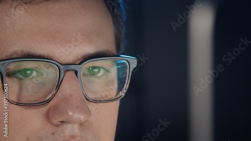 Closeup of man eyes in eyeglasses in front of the computer, gimbal pan shot left to right, concentrated look. Young man sitting working alone at night