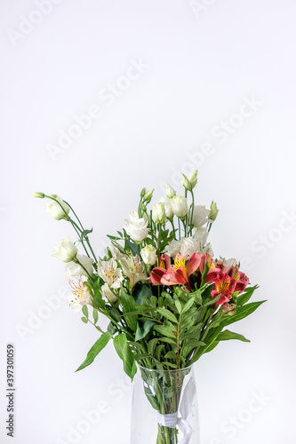 Bouquet of white and red alstroemerias and white eustomas in a glass vase. Beautiful flowers for women's day. A bouquet as a gift. White red green bouquet.